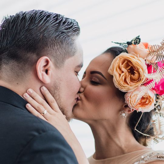 Couple kissing. She
                        is wearing a gold wedding ring and roses in her
                        hair