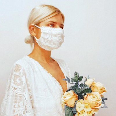 Bride wearing white lace mask and carrying a
                      bouquet of apricot roses