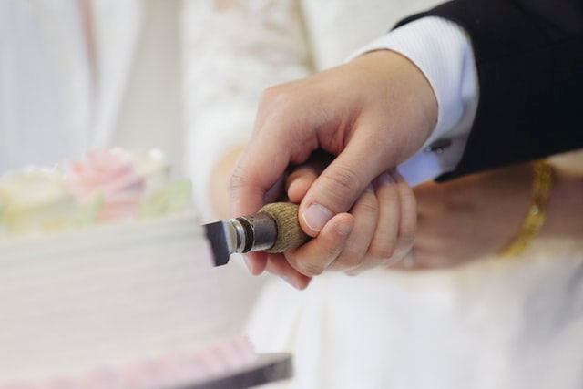 Close up of joined hands
                      cutting a cake